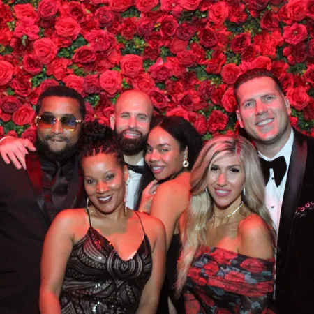Formally dressed couples at a Tampa Bay gala mirror photo booth with red rose wall